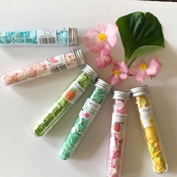 Colorful paper soap sheets in transparent cylindrical containers with floral decorations and green leaf on white background