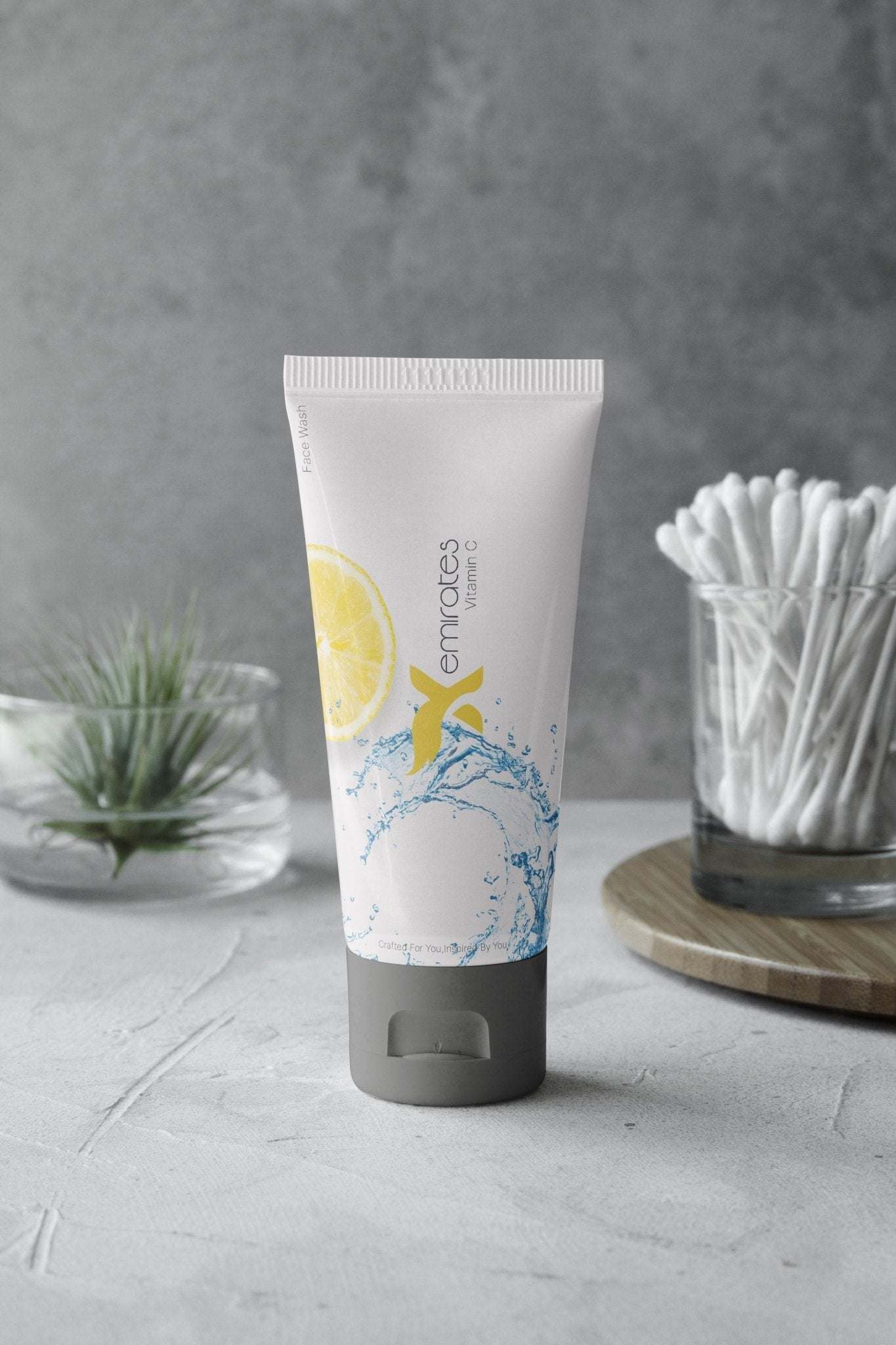 CreamXemirates skin cleansing facewash tube with natural ingredients like Tea Tree Oil and Aloe Vera on a gray surface near cotton swabs and plants